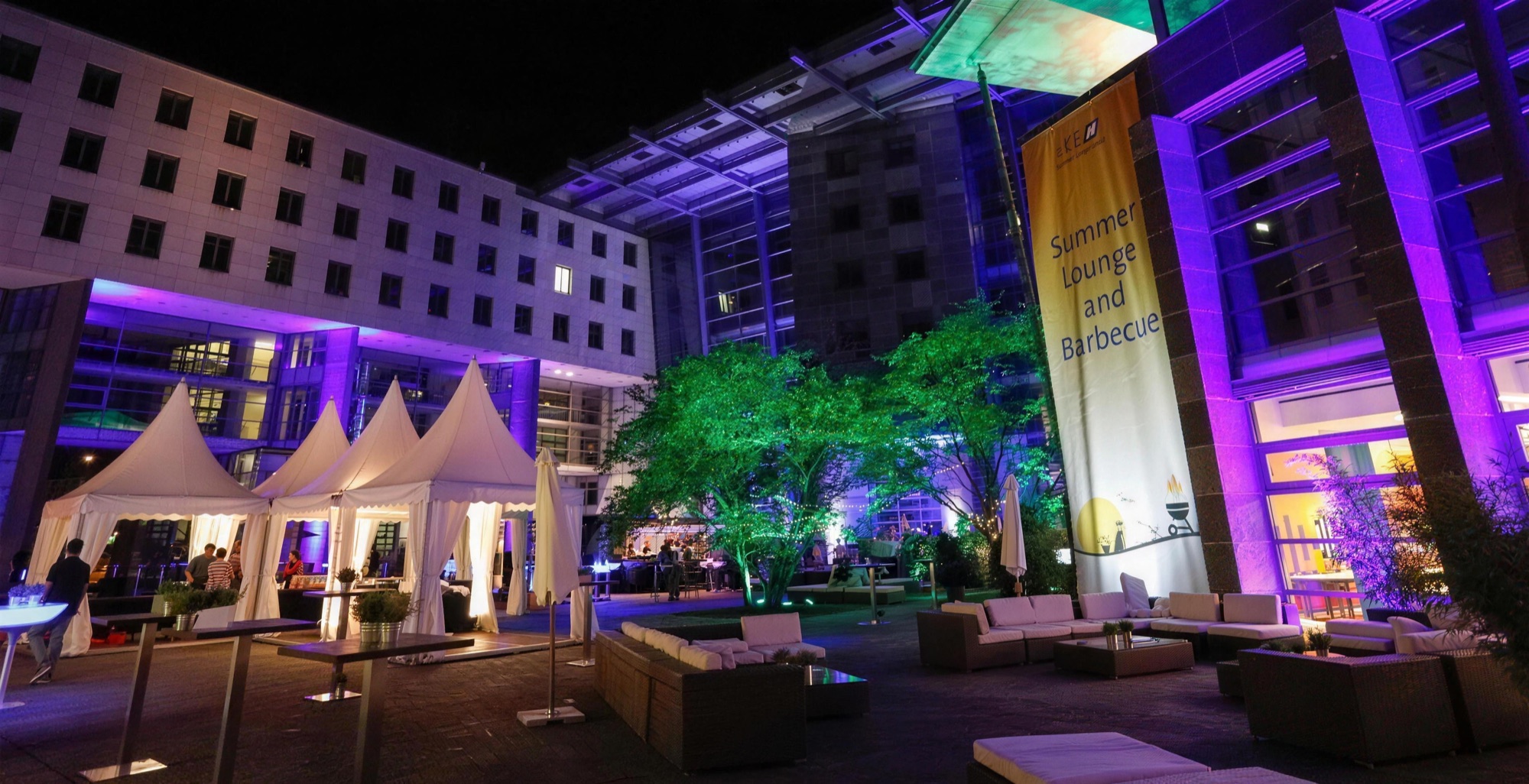 Sommerfest eines Konzerns am Abend: Pagodenzelte, Lounge-Möbel und farbige Beleuchtung im Innenhof