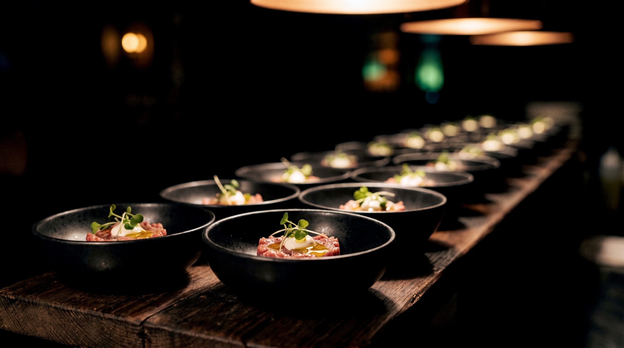 Fingerfood-Schälchen in Reihe auf langer Tafel, stimmungsvoll beleuchtet