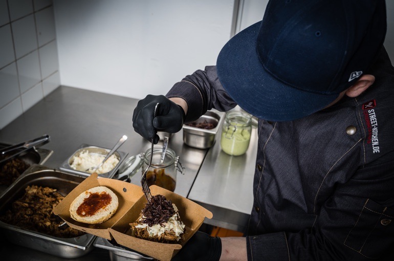 STREET-KITCHEN-Koch beim Anrichten eines Streetfood-Burgers