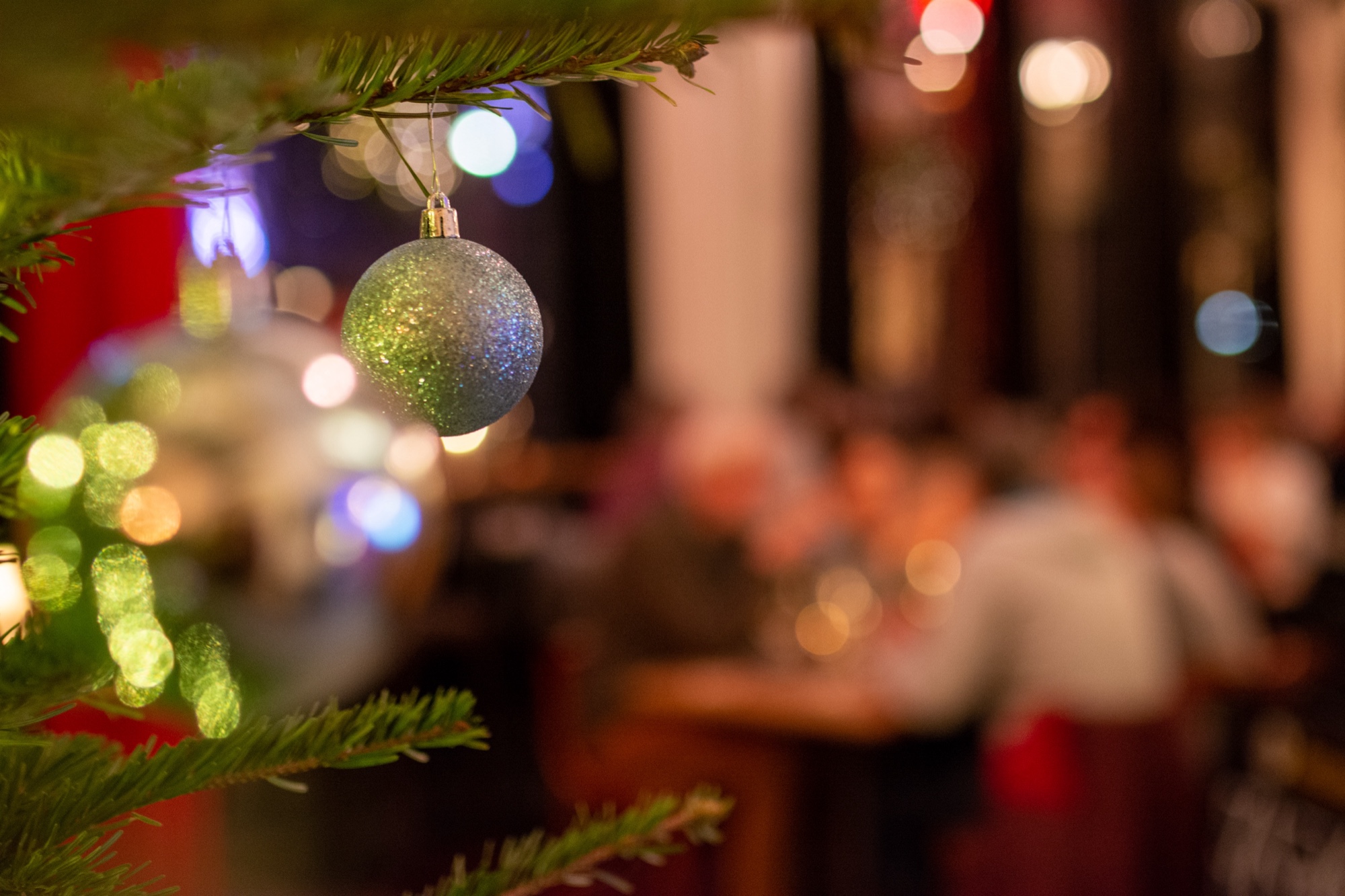 Christbaumkugel am Weihnachtsbaum im Bahnhof Blo, im Hintergrund Gäste