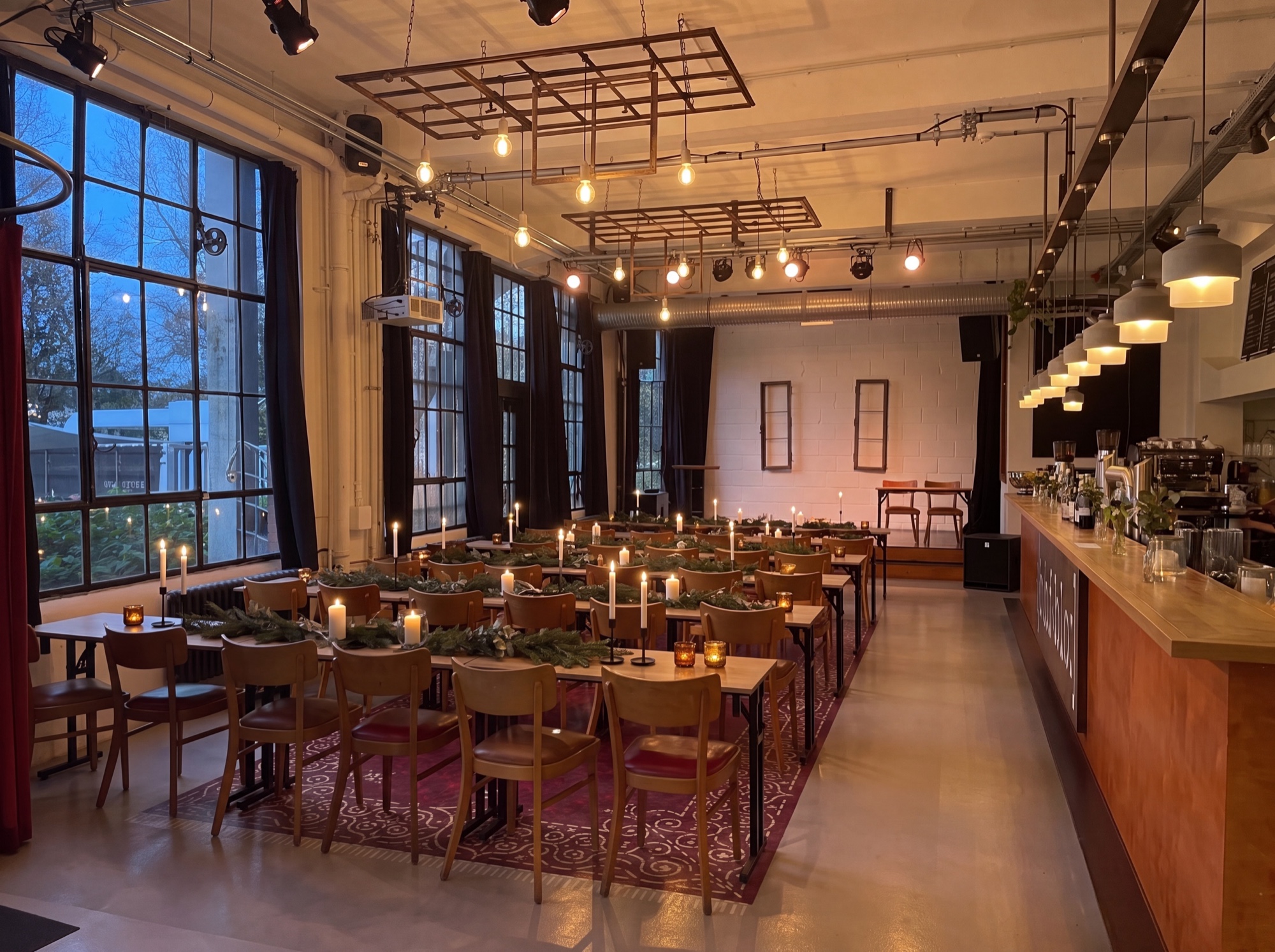 Weihnachtlich gedeckte lange Tafeln in Loft und Bar mit Bühne im Hintergrund