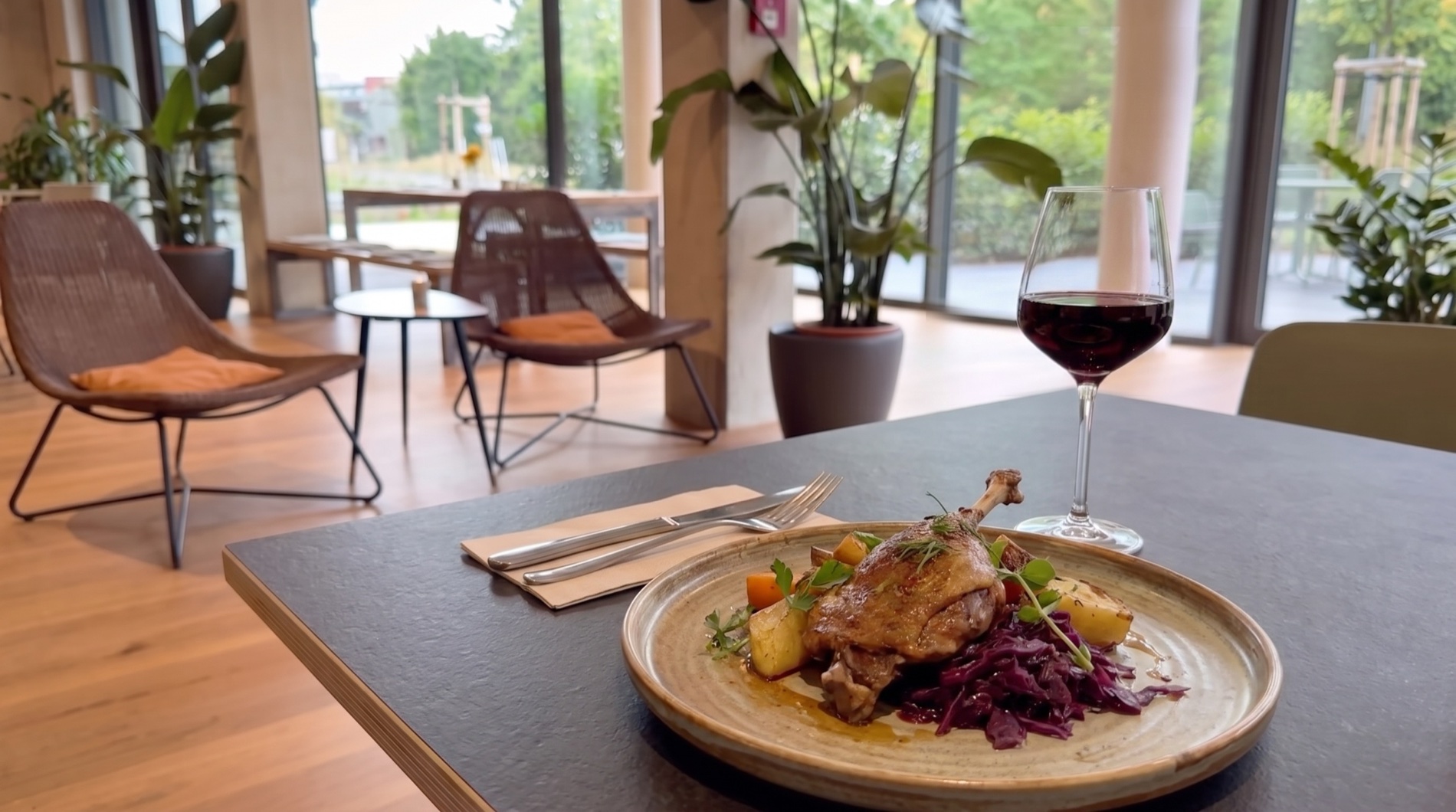 Angerichteter Teller mit Ente und Rotwein im Vordergrund, dahinter die Lounge-Ecke mit Korbsesseln im Gastraum von THE COURT