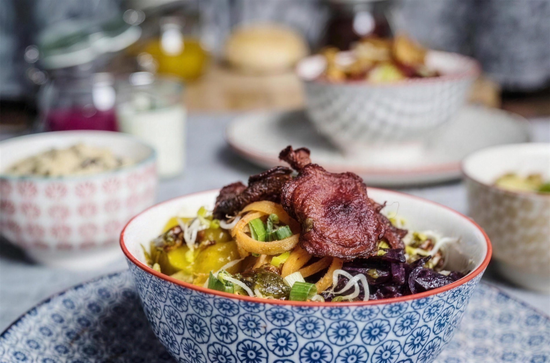 Vegane Bowl mit knusprigem Jackfruit, Möhrenspaghetti und Rotkohl, mehrere Bowls im Hintergrund