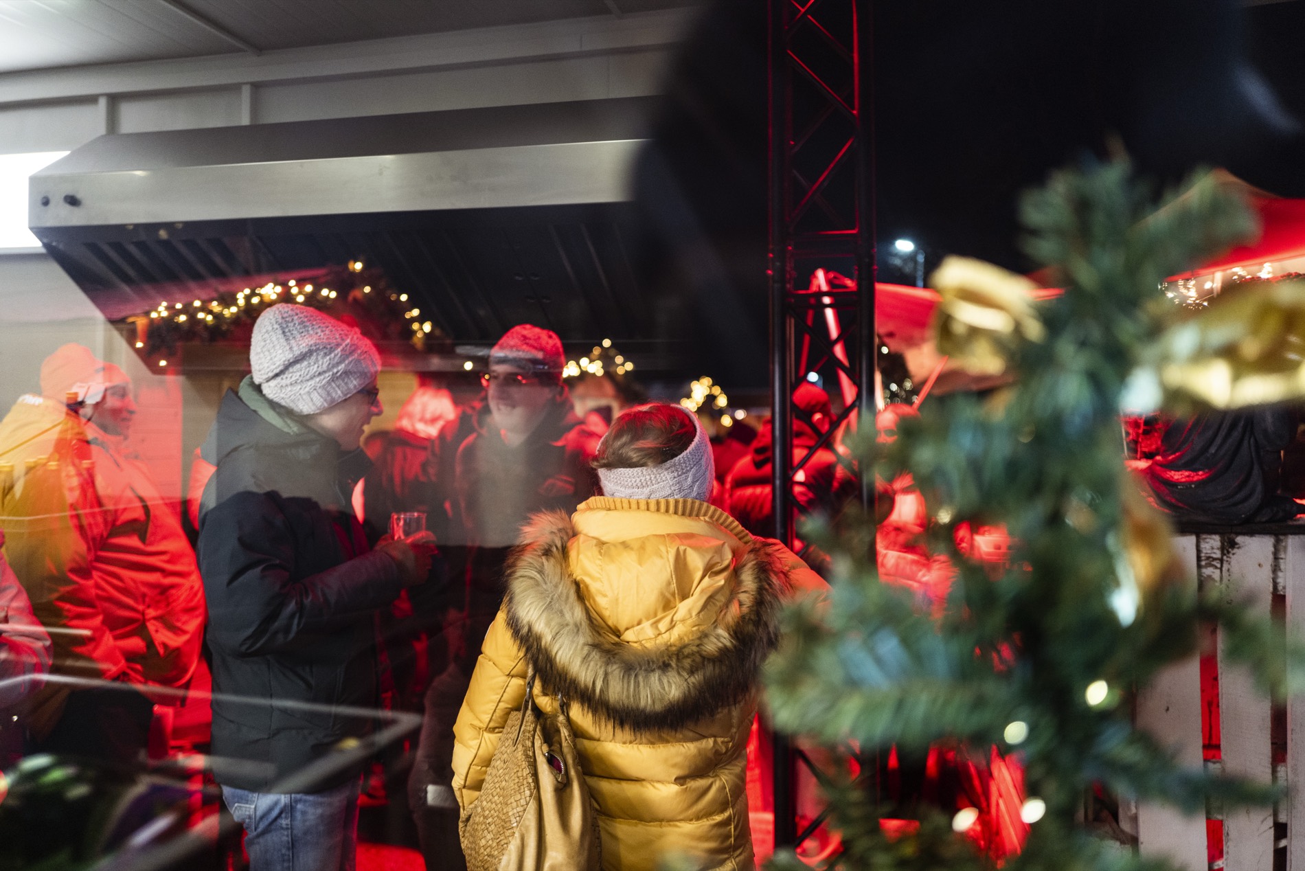 Firmen-Weihnachtsmarkt: G&auml;ste in Winterkleidung am Stand, Lichterketten und Tannengr&uuml;n