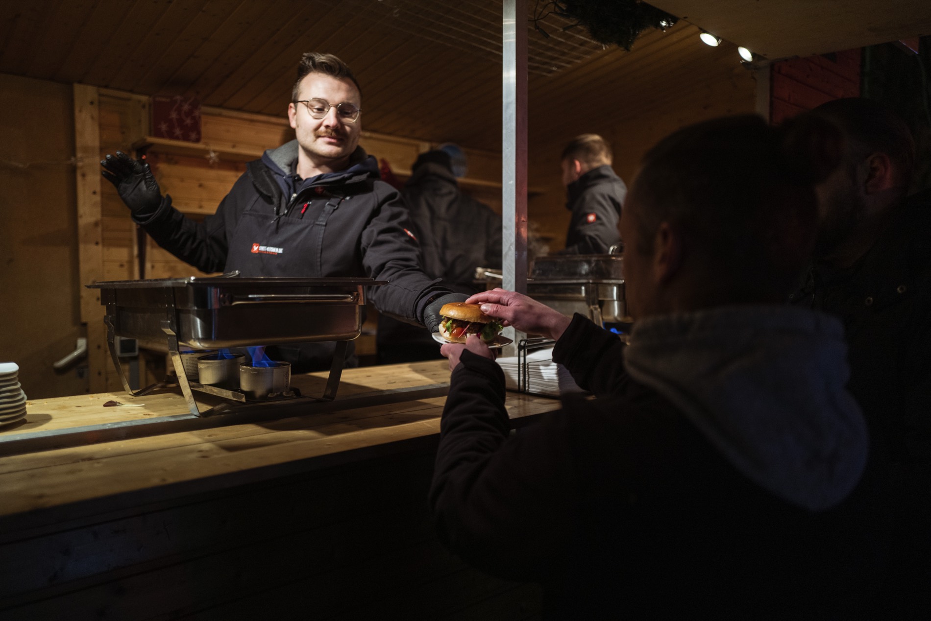 Mitarbeiter reicht einen Burger &uuml;ber die Theke der Holzh&uuml;tte