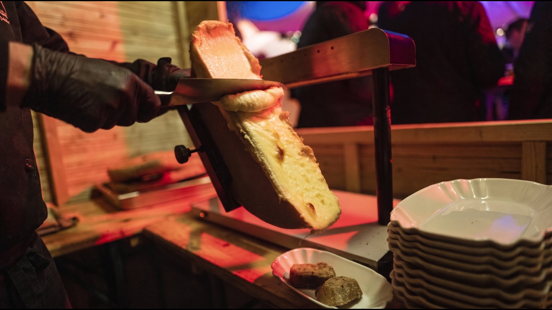 Raclette auf dem Weihnachtsmarkt: geschmolzener K&auml;se wird vom halben Laib auf Brot abgezogen