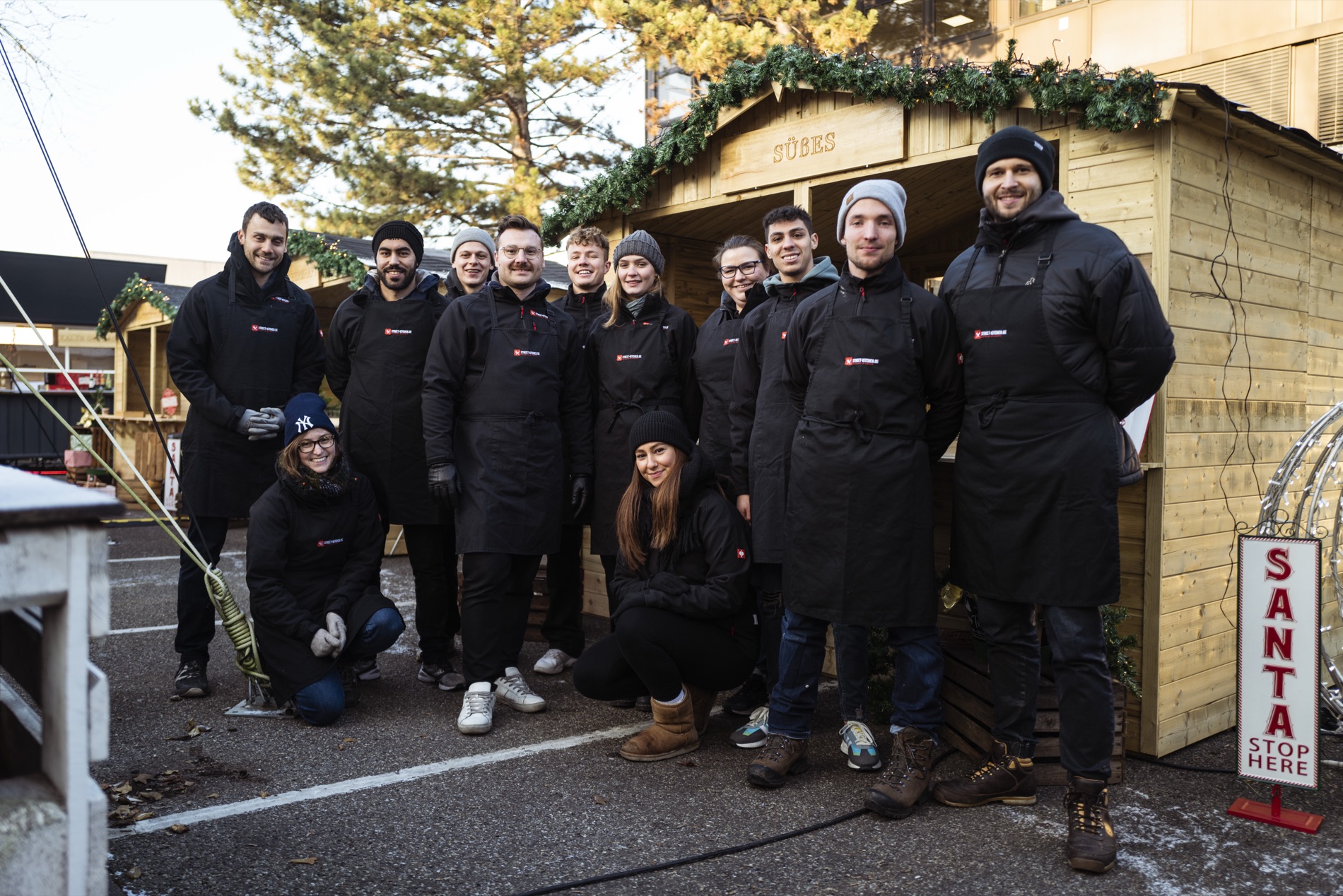 STREET-KITCHEN-Team vor der weihnachtlich geschm&uuml;ckten Holzh&uuml;tte
